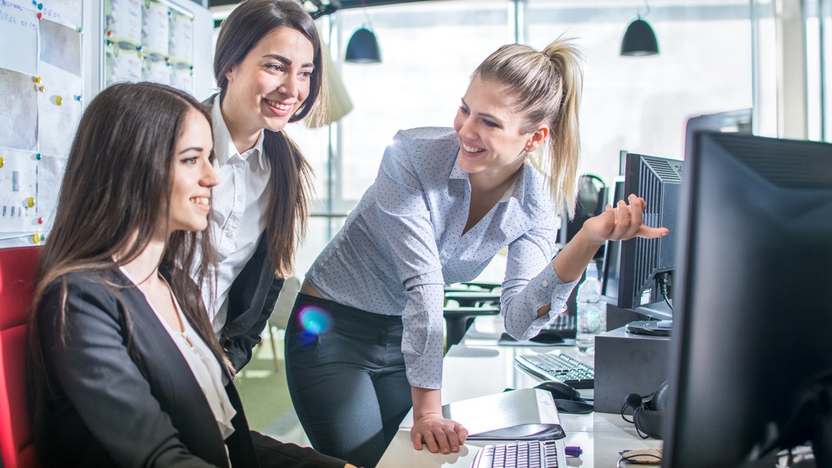 Tre colleghe sorridenti scoprono una proposta commerciale sullo schermo in un ufficio luminoso